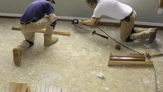 Two repair technicians kneeling on a subfloor while rebuilding a water-damaged floor